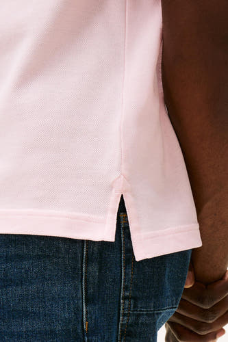 Polo rose de TOMMY HILFIGER, gros plan du bas avec des poches latérales et un jeans bleu.