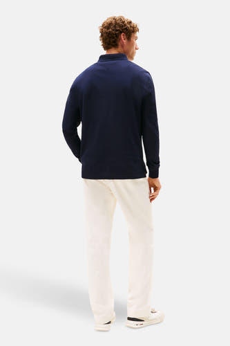 Polo bleu marine de TOMMY HILFIGER, avec des manches longues et porté avec un short blanc et des baskets, vu de dos.