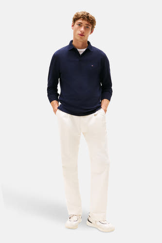 Polo bleu de Tommy Hilfiger, avec des manches longues et porté avec un short blanc et des baskets.