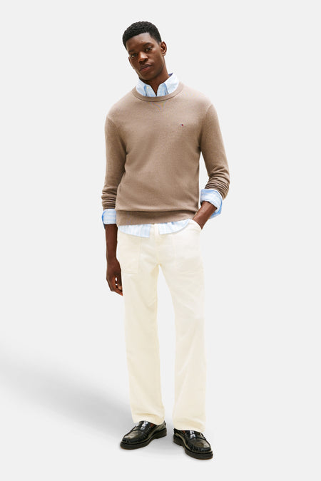 Pull beige Tommy Hilfiger avec col rond, porté sur un chemisier rayé bleu et une pantalon blanc.