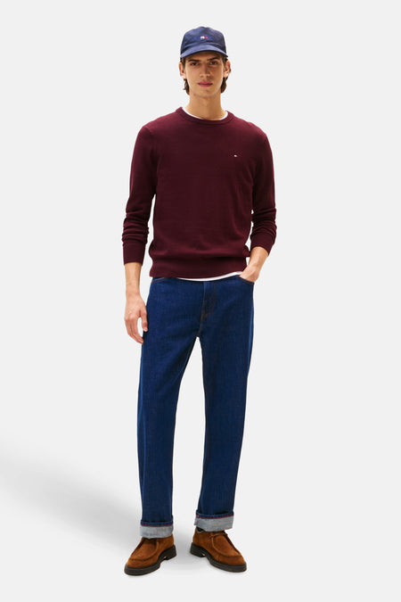 Veste de Bordeaux avec col rond de TOMMY HILFIGER, portée avec un T-shirt blanc, des jeans bleus et des chaussures marrons, associée à une casquette bleue.