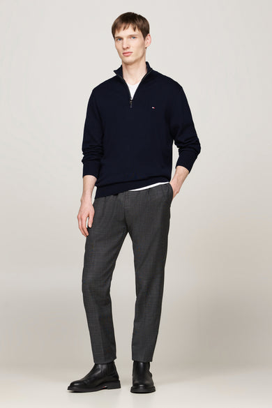 Veste bleue de TOMMY HILFIGER portée sur un t-shirt blanc, avec des pantalons en laine grise et des bottes en cuir noires.