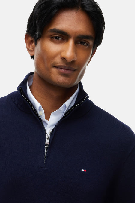 Pull à col roulé bleu de TOMMY HILFIGER, avec fermeture éclair et petit logo, porté sur une chemise blanche, gros plan sur l'avant