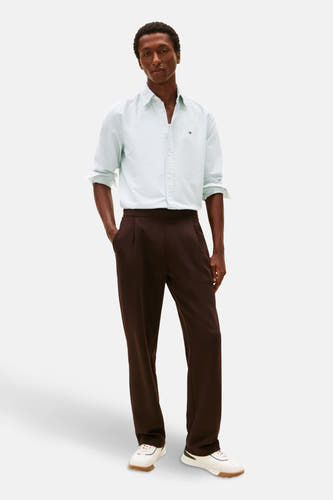 Chemise rayée verte de Tommy Hilfiger à manches longues, portée avec un pantalon marron et des baskets blanches.