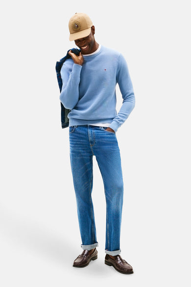 T-shirt bleu avec col rond de Tommy Hilfiger, porté avec un blouson en denim sur l'épaule, associé à des jeans et des loafers marrons.