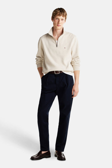 Gilet écru de TOMMY HILFIGER, porté avec un pantalon bleu marine, une ceinture marron et des loafers marrons.