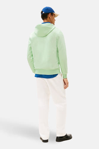Groene sweater met kap van Tommy Hilfiger, met witte broek en blauw shirt, gezien van achteren.
