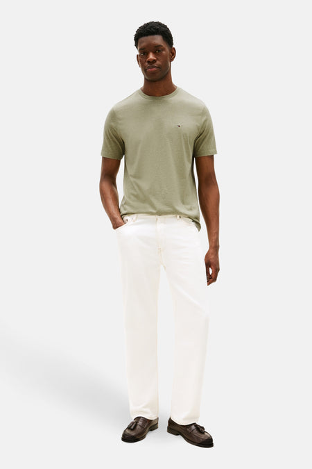 T-shirt vert de Tommy Hilfiger man courtes manches, avec un logo sur la poitrine, associé à un pantalon blanc et des loafers marrons.
