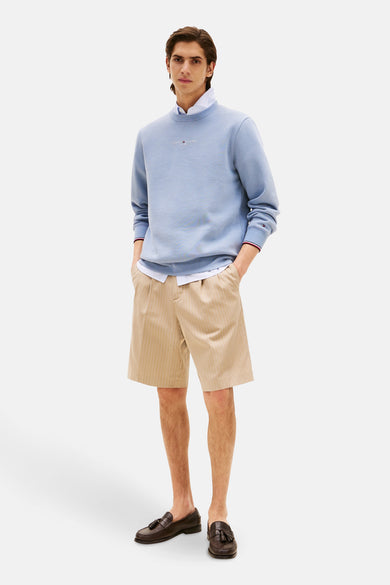 Pull-over bleu Tommy Hilfiger porté avec une chemise et des short rayés avec des loafers marrons.