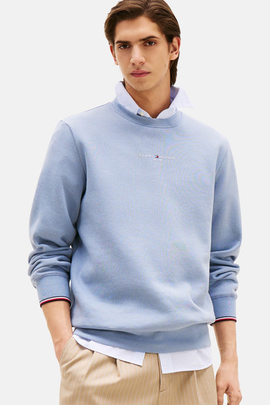 Pull-over bleu de TOMMY HILFIGER, porté avec un chemise blanche et un pantalon rayé.