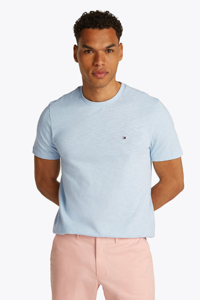 T-shirt à manches courtes bleu clair de TOMMY HILFIGER avec col rond et petit logo sur la poitrine, porté par un mannequin en pantalon rose