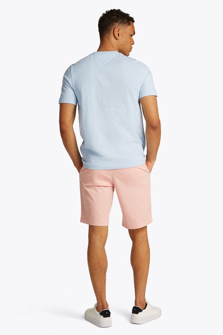 T-shirt à manches courtes bleu clair de TOMMY HILFIGER, dos visible sur un mannequin portant un short rose et des baskets blanches