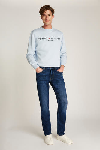 Jean denim bleu marine Tommy Hilfiger, porté avec une chemise bleue claire et des baskets blanches.