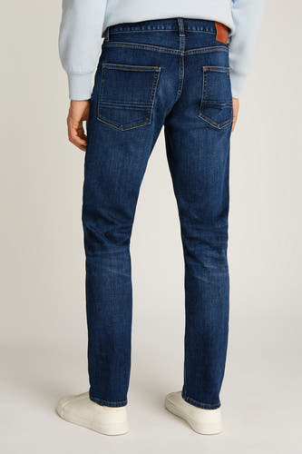 Jean droit en denim bleu marine de TOMMY HILFIGER, vu de l'arrière avec des baskets beige et une chemise bleue claire.
