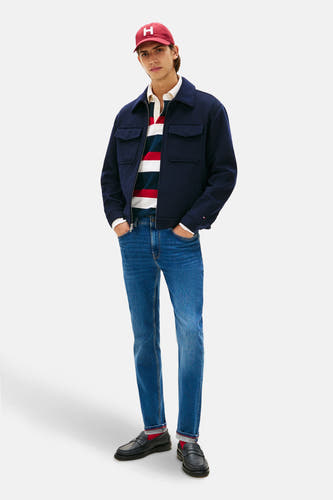 Jean slim fit de TOMMY HILFIGER, avec un lavage denim bleu moyen, associé à un t-shirt rugby, une veste et des loafers.