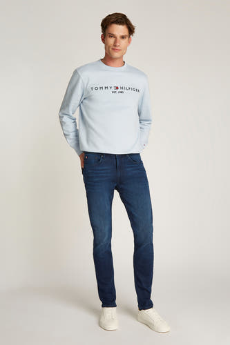 Jean denim bleu foncé Tommy Hilfiger, porté avec un sweat-shirt bleu clair et des baskets blanches.