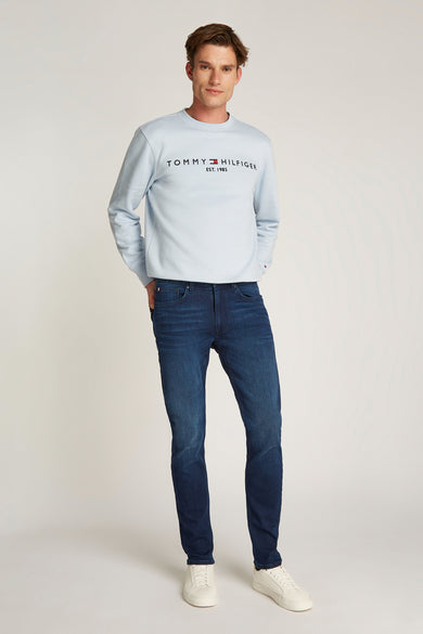 Jean denim bleu foncé Tommy Hilfiger, porté avec un sweat-shirt bleu clair et des baskets blanches.