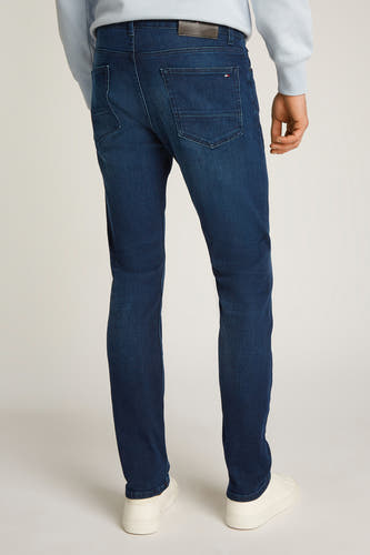 Jean droit en denim bleu marine de Tommy Hilfiger, arrière-plan montré avec des baskets blanches et un pull bleu clair.