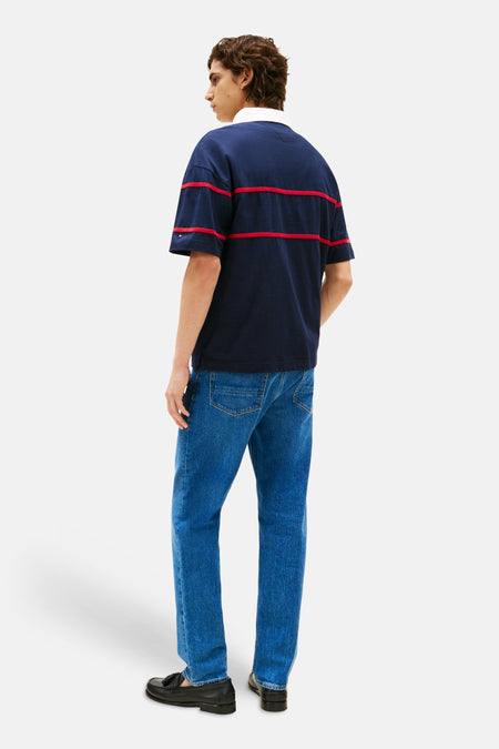 Polo bleu à manches courtes de Tommy Hilfiger, avec des rayures rouges et porté avec un jean bleu et des mocassins noirs.