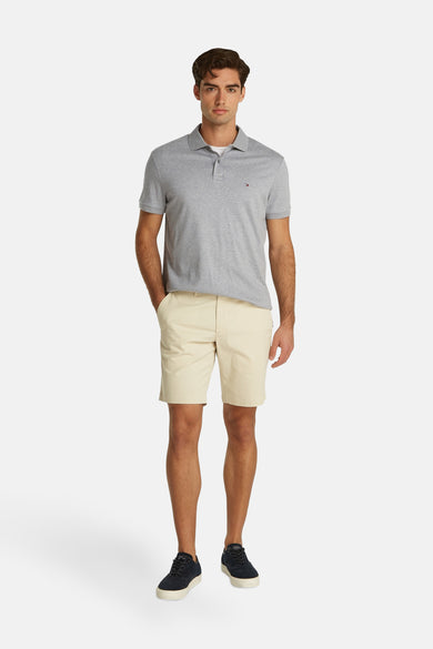 Polo gris de TOMMY HILFIGER, texture rayée, petit logo sur la poitrine, le modèle porte un short beige et des baskets foncées, vue de face.