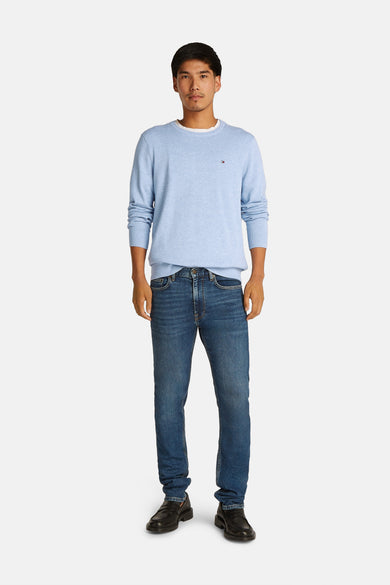Pull à col rond bleu clair de TOMMY HILFIGER, avec petit logo sur la poitrine, porté avec un jean bleu foncé et des chaussures noires, vue de face.