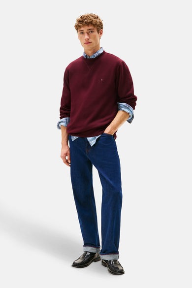 Pull-over rouge à col rond de TOMMY HILFIGER, porté sur une chemise à carreaux et associé à des jeans bleus marine et des loafers noirs.