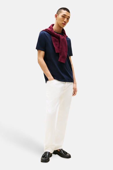 T-shirt bleu à manches courtes de Tommy Hilfiger, associé à un pantalon blanc et une veste bordeaux boutonnée nonchalamment.