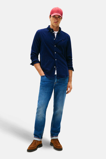 Chemise bleue de TOMMY HILFIGER, portée avec un T-shirt blanc, des jeans et des chaussures en cuir, avec une casquette rouge.