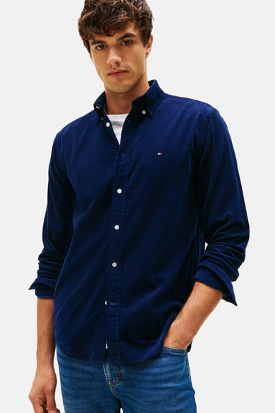 Chemise bleue corduroy de Tommy Hilfiger, avec des manches longues et un t-shirt blanc en dessous.
