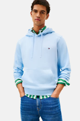 Pull-over bleu avec capuche de Tommy Hilfiger, porté avec un chemisier rayé et des pantalons de travail.