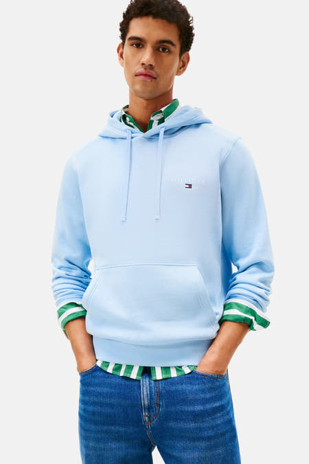 Pull-over bleu avec capuche de Tommy Hilfiger, porté avec un chemisier rayé et des pantalons de travail.