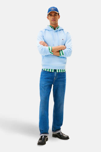 Pull-over bleu Tommy Hilfiger avec un capuchon, à longues manches, associé à une chemise à rayures vertes et des jeans.