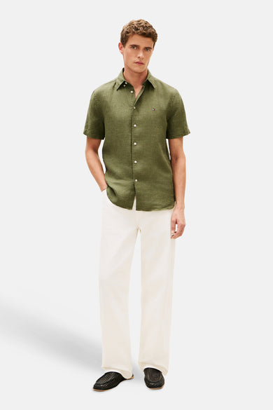 Groen overhemd van TOMMY HILFIGER, korte mouwen, met witte knopen en een geborduurde logo, gecombineerd met een witte broek en zwarte instappers.
