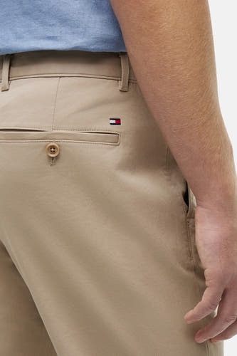 Chino beige de TOMMY HILFIGER avec sergé, poche arrière à bouton, petit logo drapeau et le bras d'un homme.