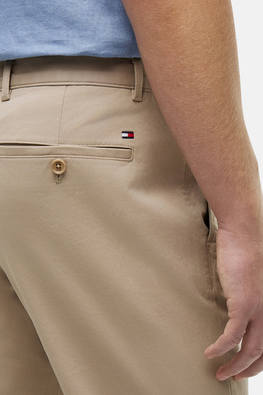 Chino beige de TOMMY HILFIGER avec sergé, poche arrière à bouton, petit logo drapeau et le bras d'un homme.