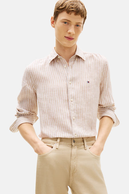 Beige gestreept overhemd van Tommy Hilfiger met lange mouwen en zichtbaar logo op de borst, gedragen met een beige broek.
