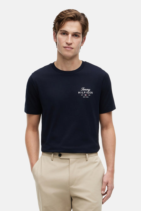 T-shirt bleu marine de TOMMY HILFIGER avec logo sur la poitrine, porté par un homme avec un pantalon beige.