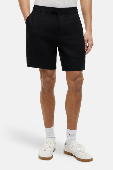 Bermuda noir Tommy Hilfiger, avec cordon de serrage et poches, porté avec un t-shirt blanc et des baskets blanches.