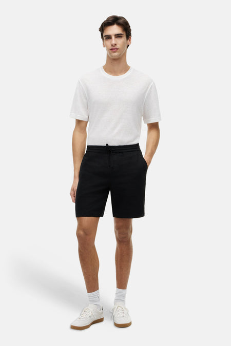 Zwarte bermuda van Tommy Hilfiger, met trekkoord en zakken, gedragen met een wit T-shirt en witte sneakers.