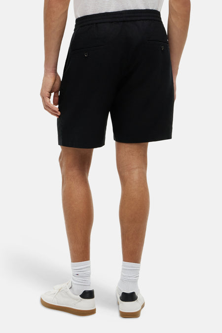 Bermuda noire Tommy Hilfiger, dos, avec poches à boutons et baskets blanches avec chaussettes.
