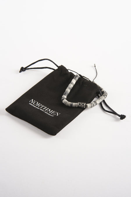 Bracelet gris de NORTHMEN, à côté d'un sac en tissu noir avec cordon, sur un fond blanc.