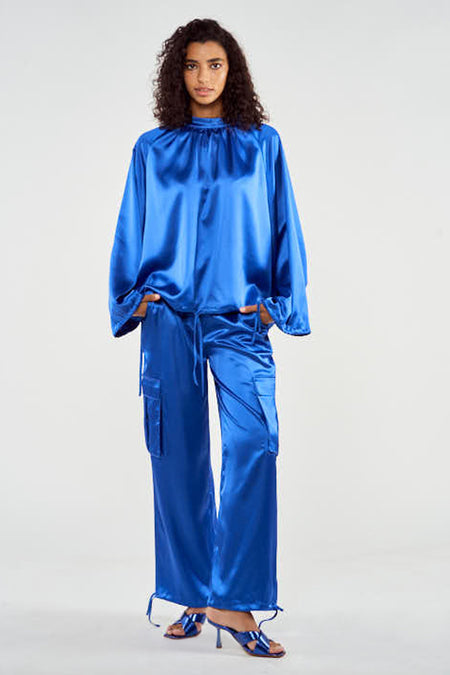 Pantalon de travail bleu de NOOR BY NORA GHARIB, avec poches et cordons sur les bords, porté avec des bottes bleues.