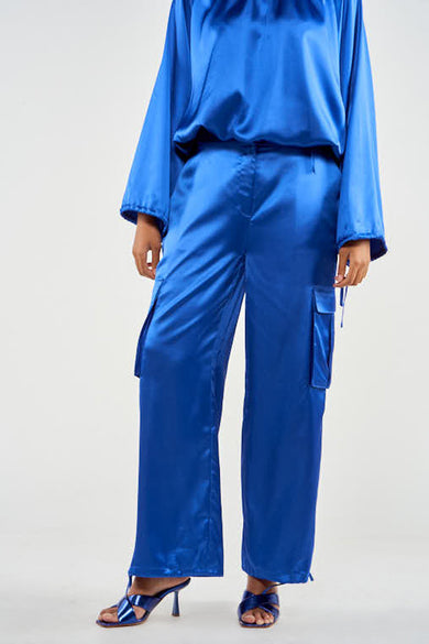 Pantalon cargo bleu de NOOR BY NORA GHARIB, avec de grands poches, associé à une chemise coordonnée et des sandales bleues.