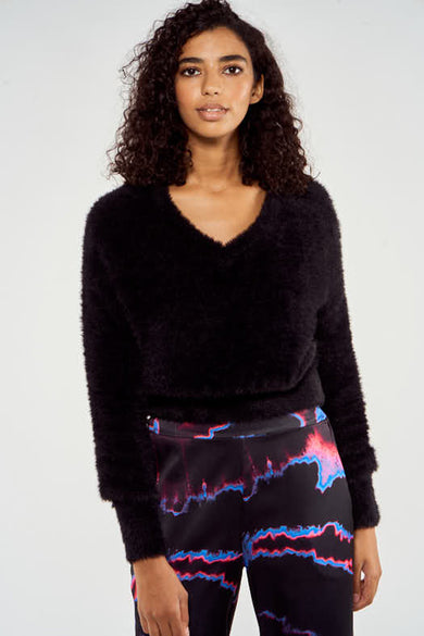 Pull noir à col V de NOOR BY NORA GHARIB, avec longues manches et une douce texture, associé à un pantalon imprimé.