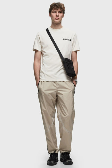 T-shirt écru de NAPAPIJRI, avec des manches courtes et un petit logo sur la poitrine, porté avec une sacoche cross-body noire et un pantalon beige.