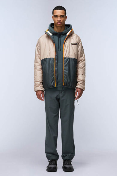 Vestes de pluie beige de NAPAPIJRI, avec un bloc de couleur vert foncé sur la poitrine, portées sur une hoodie verte et un pantalon.