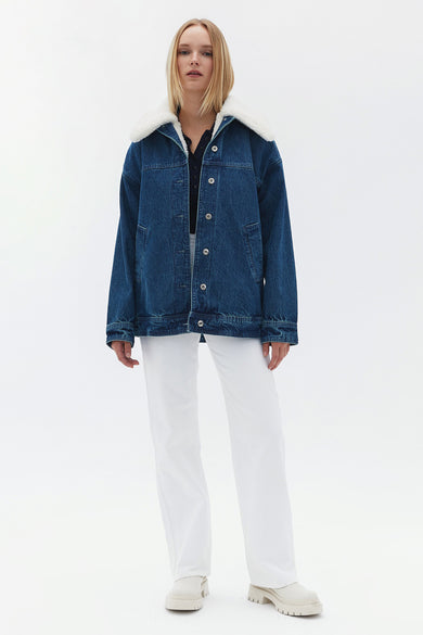 Jean en denim de OXXO, avec une doublure blanche sur le col, associé à un short blanc et des chaussures.