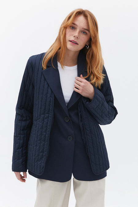 Manteau court bleu d'OXXO avec fermeture à boutons, détail en fausse fourrure et pantalon léger.