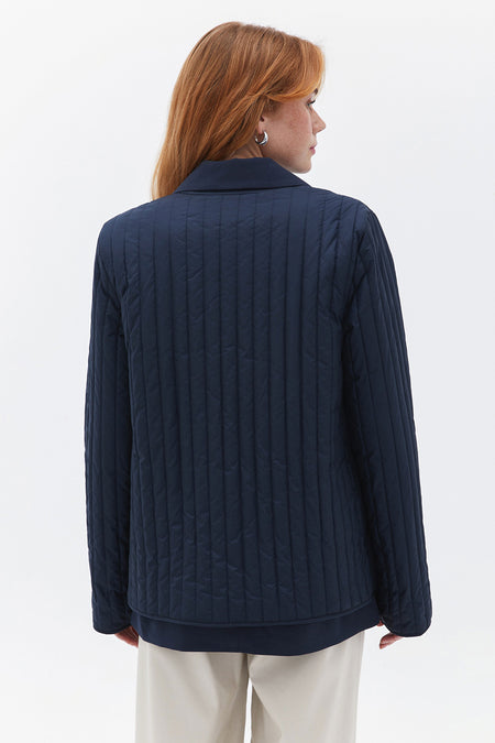 Manteau bleu d'OXXO avec quilting vertical sur un modèle vu de derrière.
