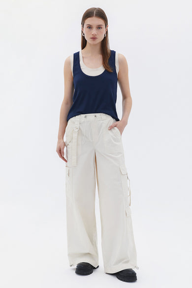 T-shirt bleu d'OXXO, porté avec un pantalon beige à larges pinces et des chaussures noires.